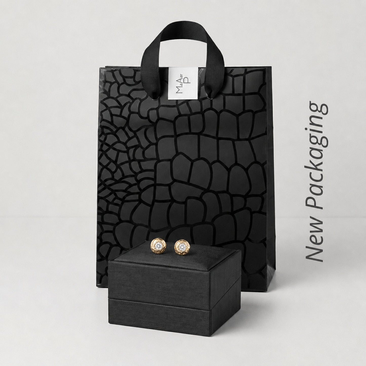 Presentación de empaque de lujo para joyería que incluye un estuche rígido negro mate con los pendientes de oro y una bolsa de regalo negra con textura de piel de cocodrilo.