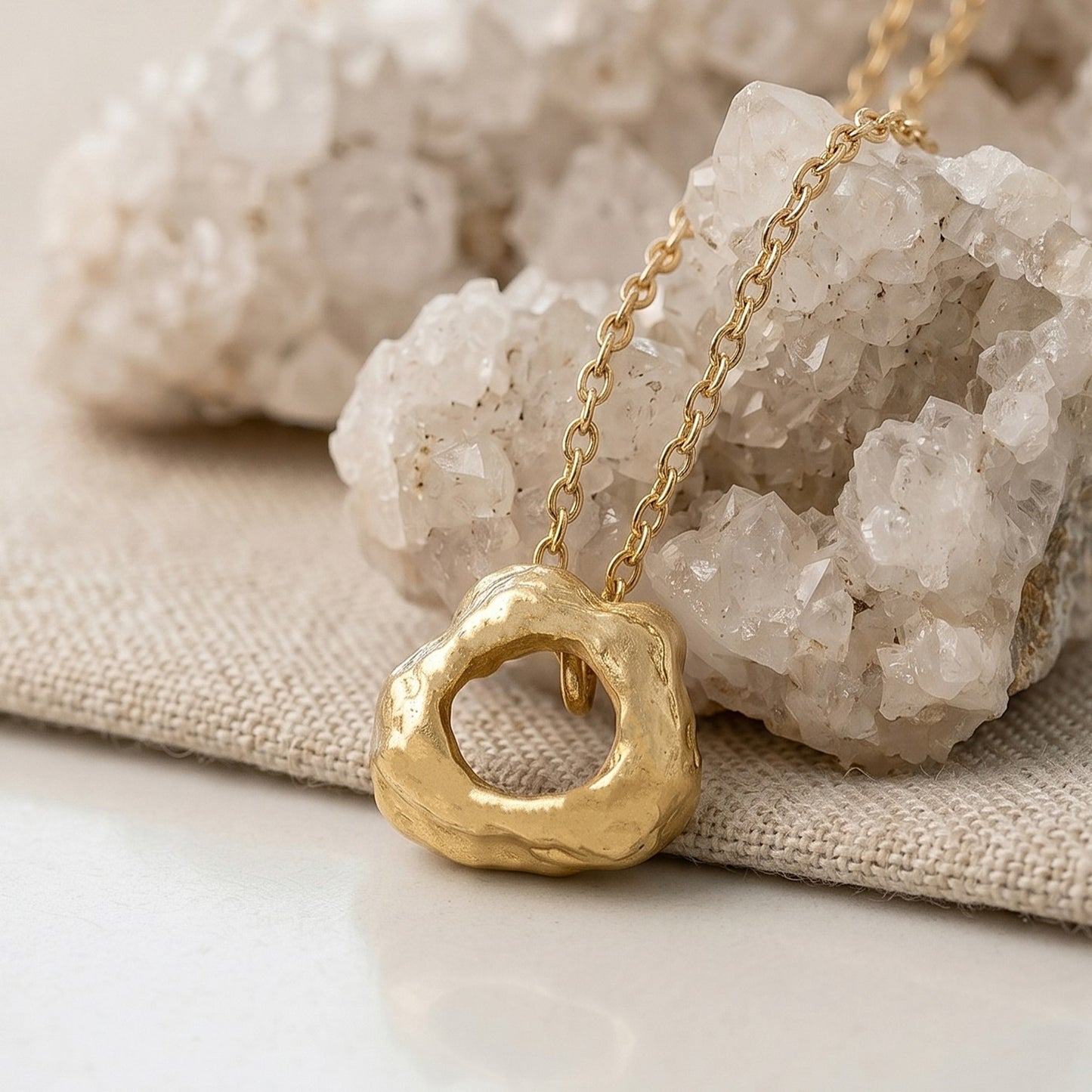 Colgante de oro vermeil apoyado sobre cristales de cuarzo blanco y una base de lino beige, resaltando su brillo dorado y textura orgánica.