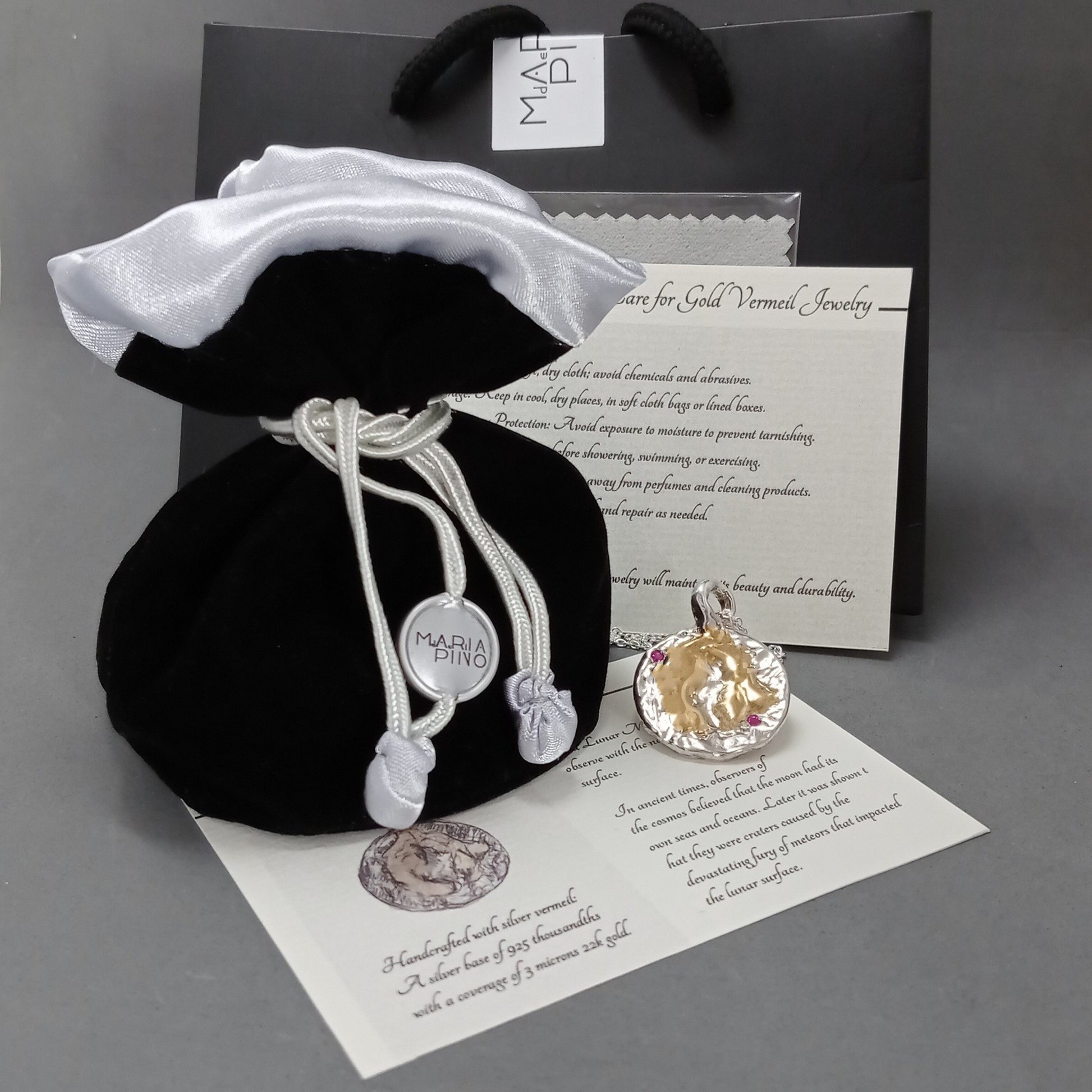 Colgante Mares de Luna en plata, oro vermeil y rubíes naturales junto a bolsa, estuche y tarjeta de cuidado de joyería.