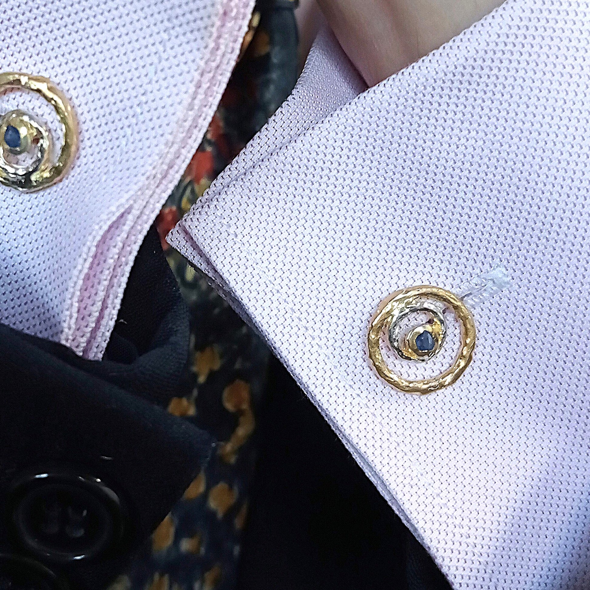 Primer plano de gemelo de diseño orgánico en oro y plata colocado en el puño de una camisa rosa.