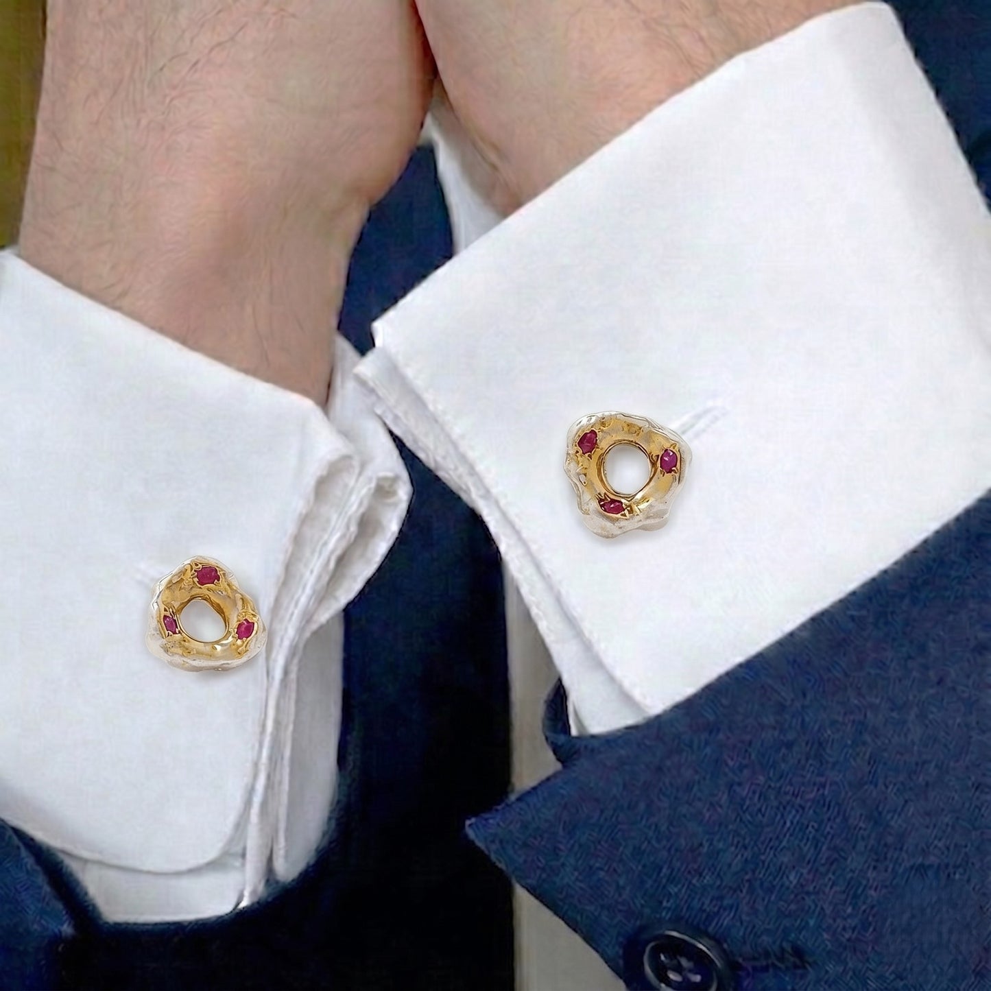 Gemelos artesanales de plata y oro vermeil con rubíes puestos en puños de camisa blanca y chaqueta azul.