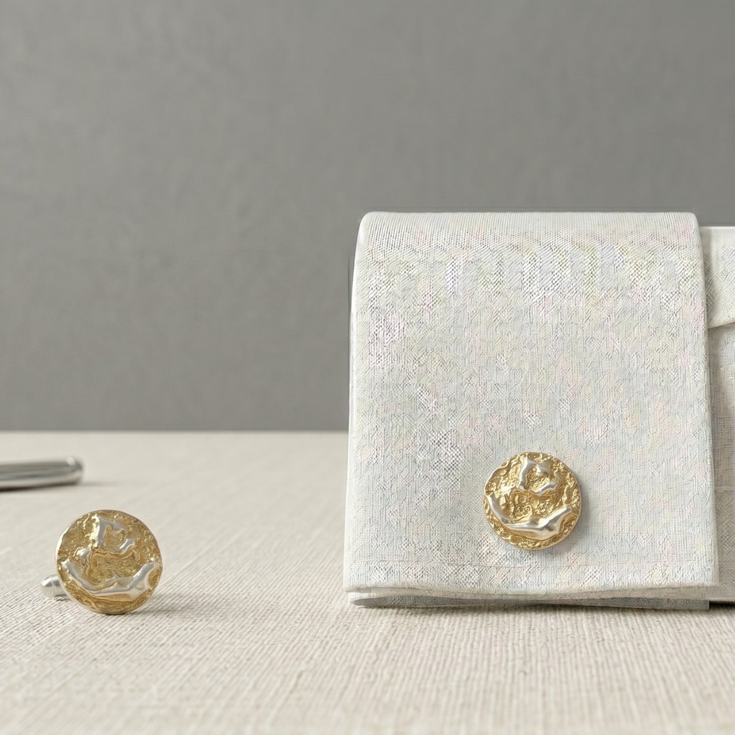 Gemelos artesanales de oro vermeil con textura orgánica escultórica sobre camisa blanca elegante, joyería masculina inspirada en superficies cósmicas y formas minerales.