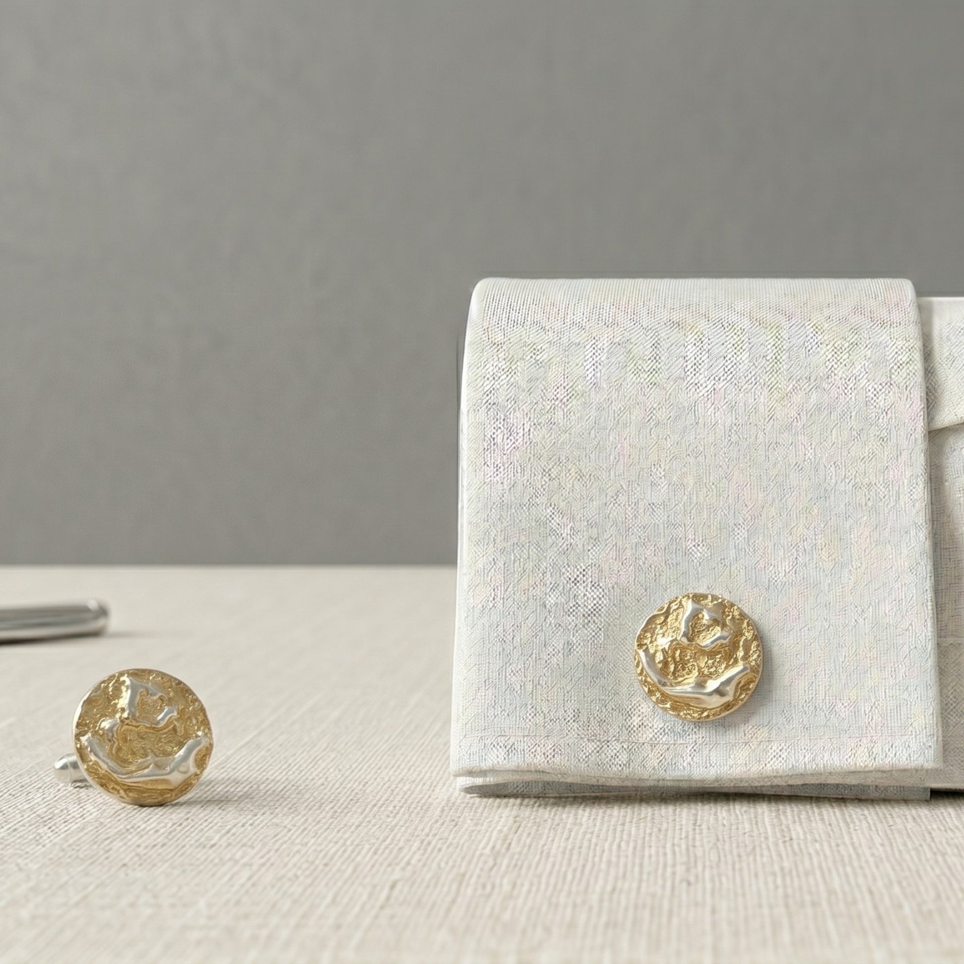 Gemelos artesanales de oro vermeil con textura orgánica escultórica sobre camisa blanca elegante, joyería masculina inspirada en superficies cósmicas y formas minerales.