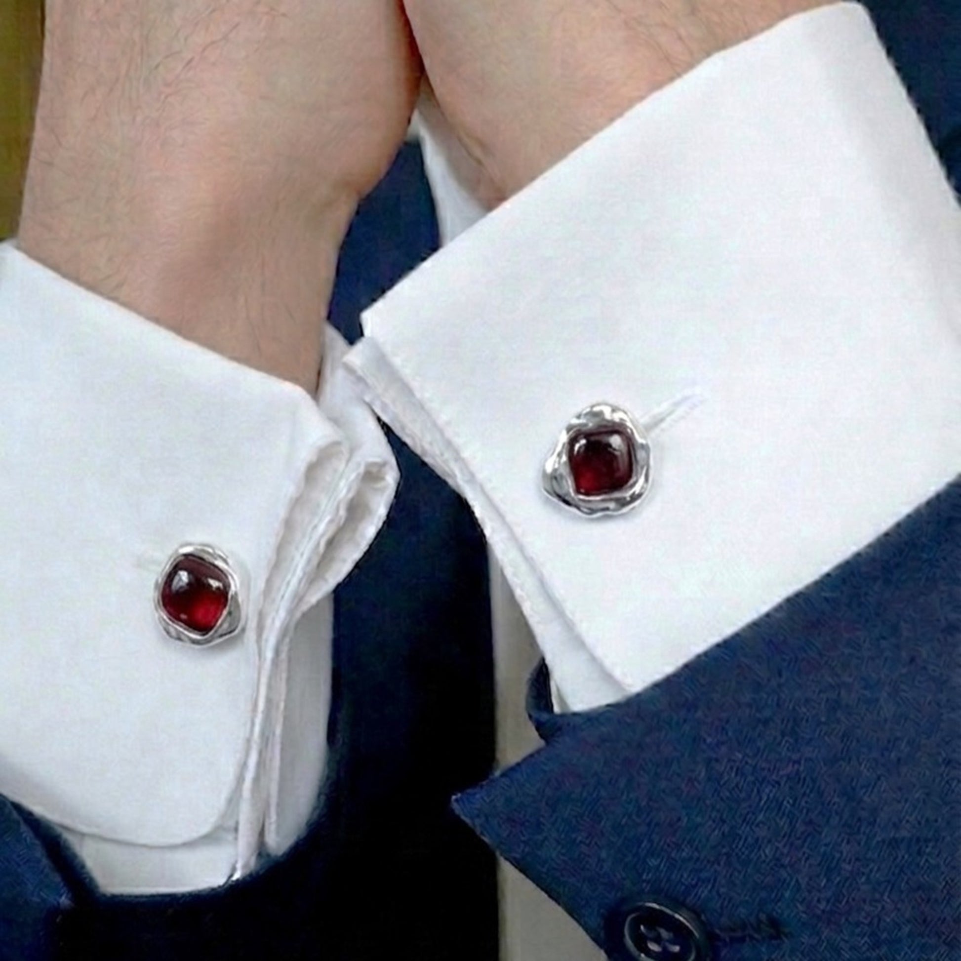 Hombre vistiendo camisa blanca y chaqueta azul mostrando los gemelos de granate en los puños.