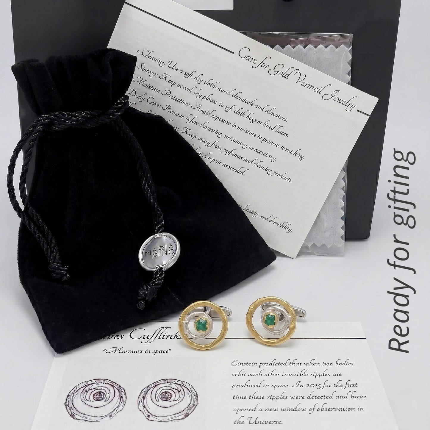 Un par de gemelos de esmeralda de lujo en su embalaje de regalo, incluyendo una bolsa de terciopelo negro y una tarjeta de instrucciones de cuidado.