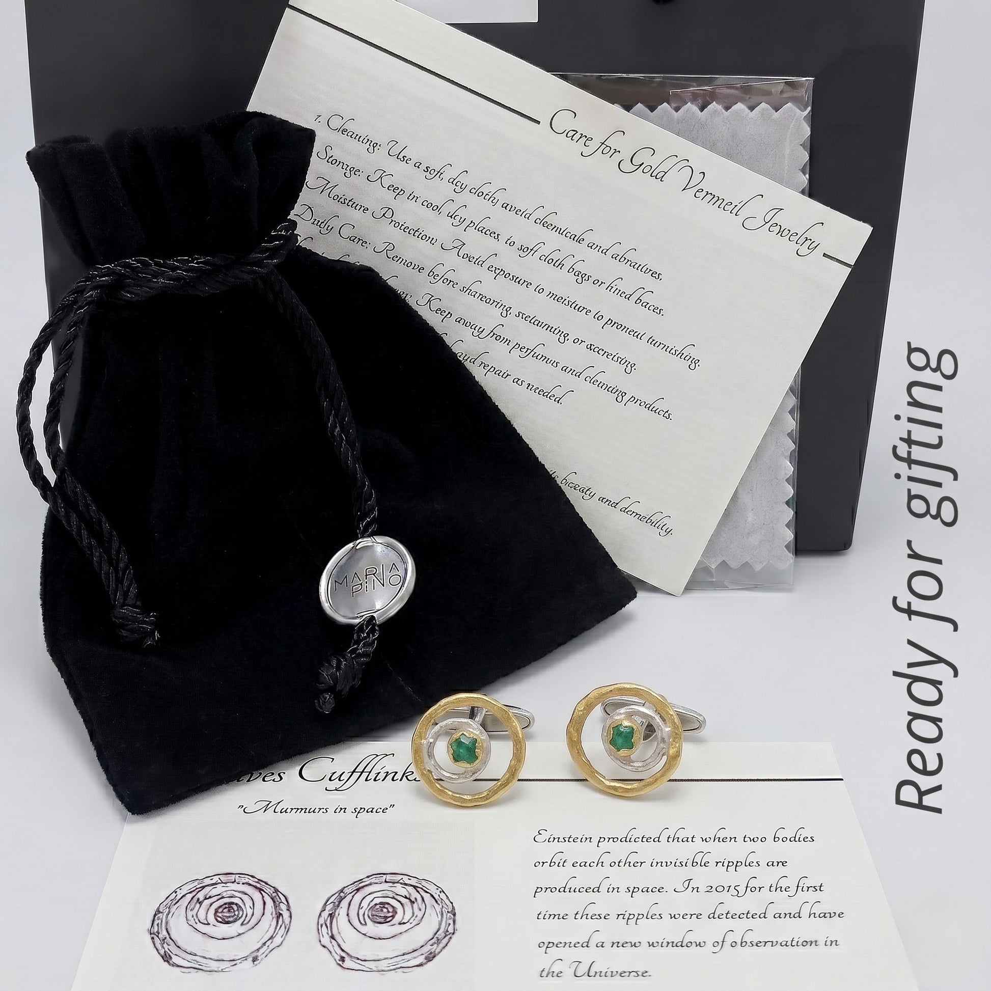 Un par de gemelos de esmeralda de lujo en su embalaje de regalo, incluyendo una bolsa de terciopelo negro y una tarjeta de instrucciones de cuidado.