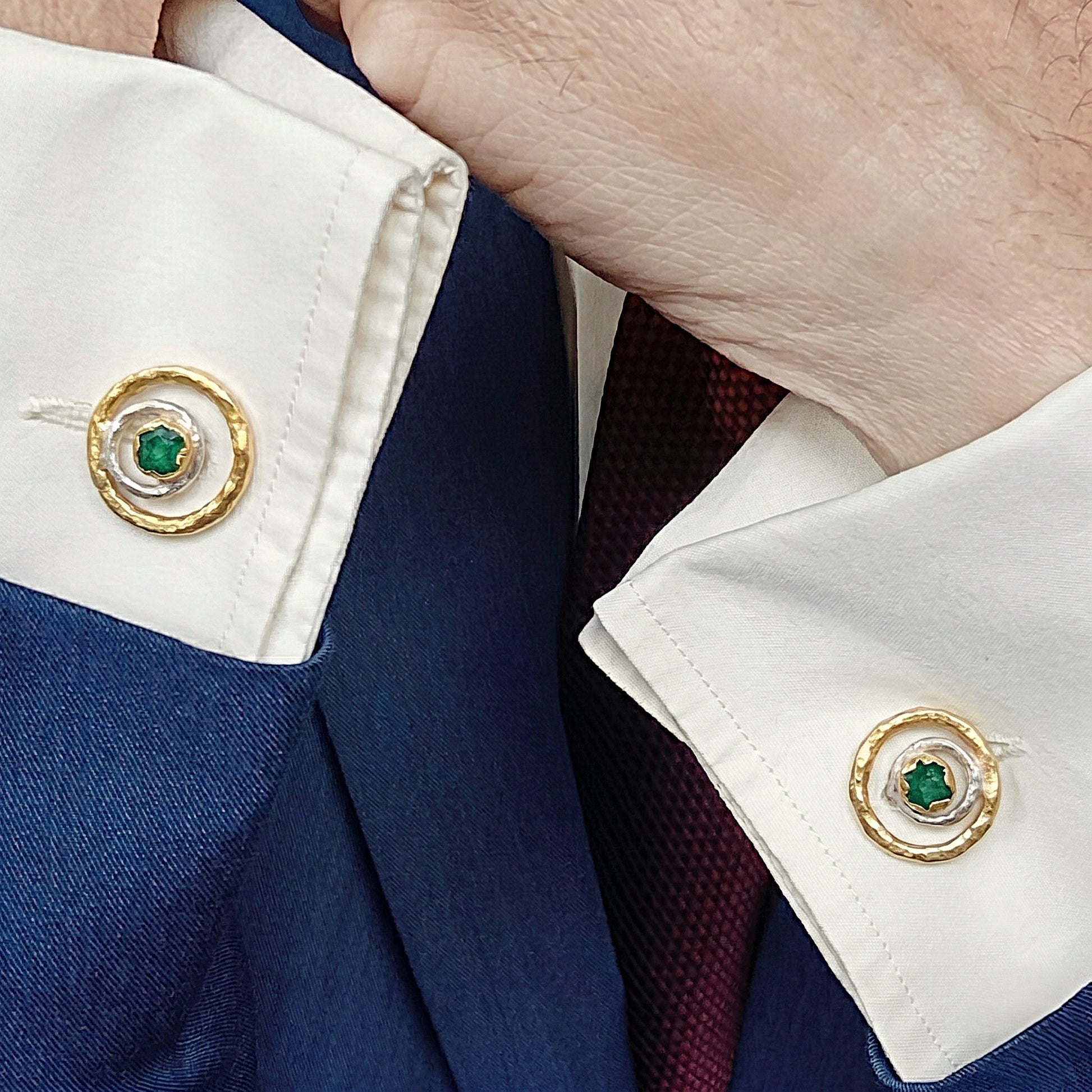 Primer plano de un hombre que lleva gemelos de esmeralda cruda en una camisa de vestir blanca, con una chaqueta azul marino y una corbata burdeos.