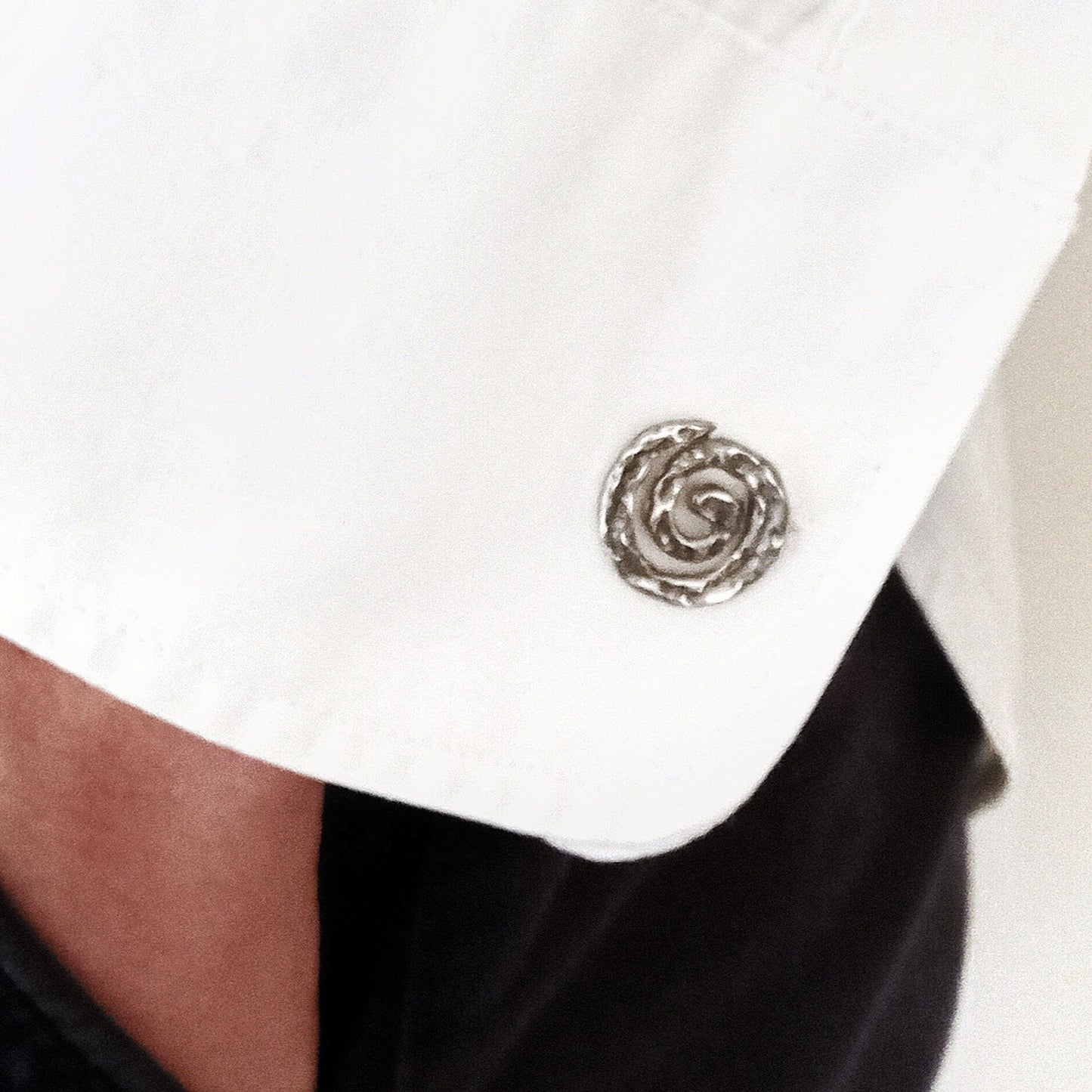 Primer plano de un gemelo de plata en forma de espiral colocado en el puño de una camisa blanca de vestir.