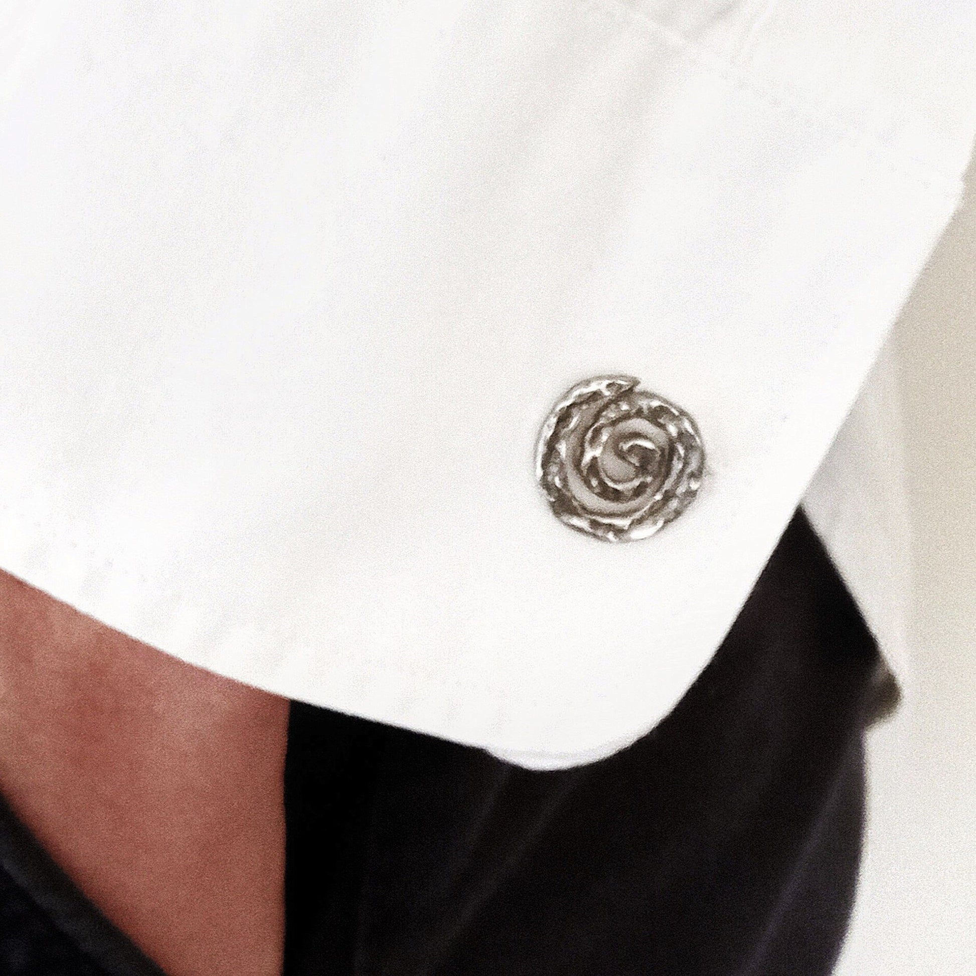 Primer plano de un gemelo de plata en forma de espiral colocado en el puño de una camisa blanca de vestir.