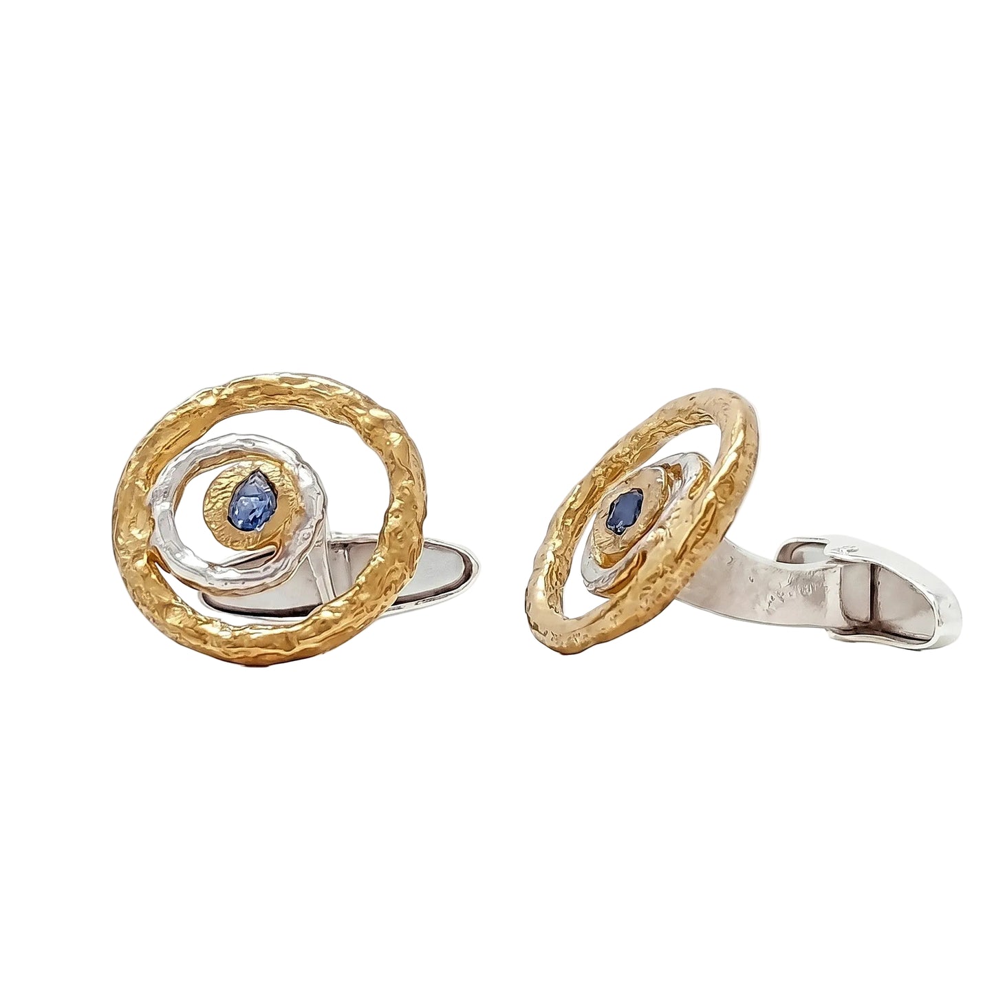 Par de gemelos artesanales redondos de oro y plata con zafiro azul central sobre fondo blanco.
