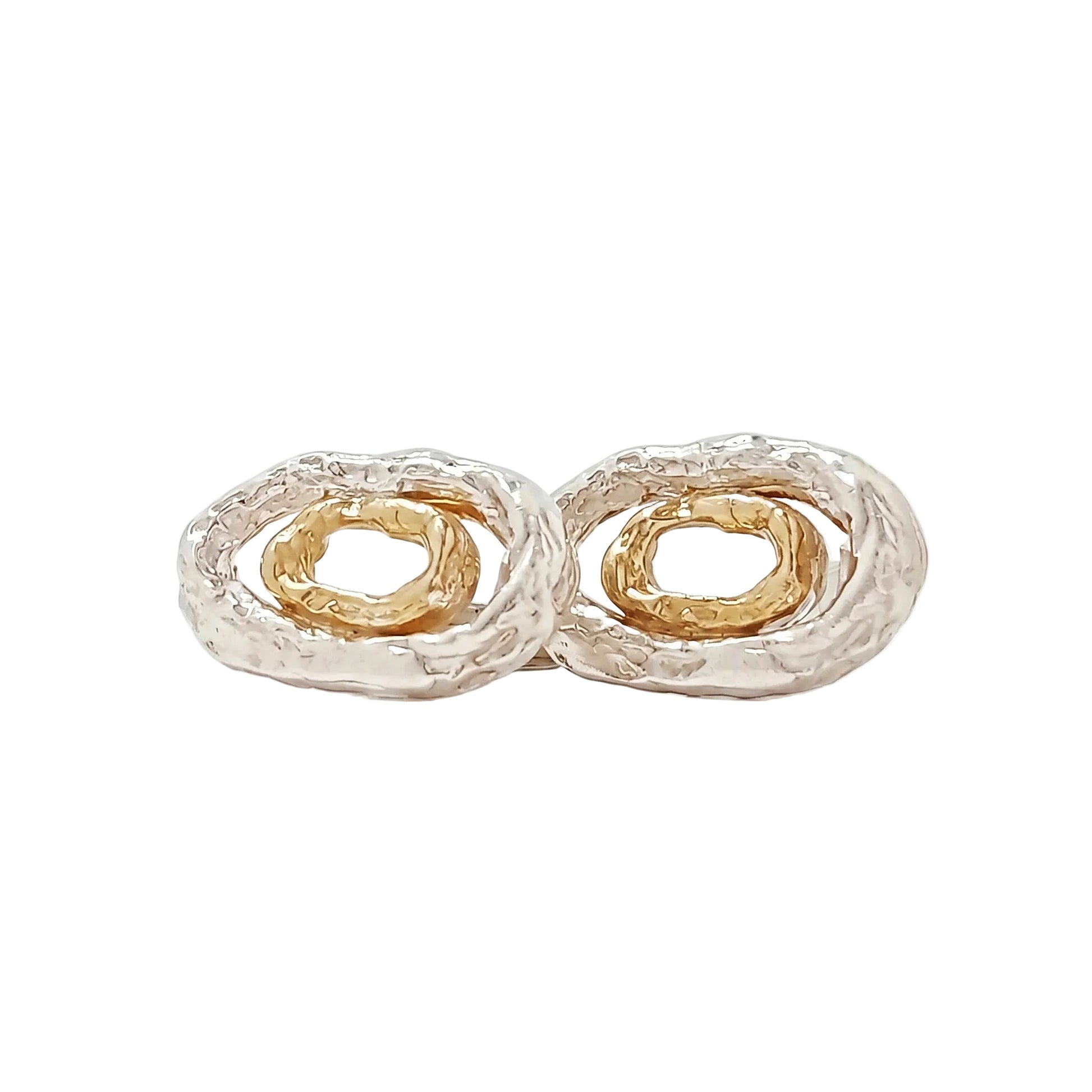 Primer plano de estudio de un par de gemelos de diseño elíptico en plata de ley texturizada con anillos interiores concéntricos de oro vermeil. Uno está de frente y el otro de perfil para mostrar el mecanismo de cierre de barra T. Fondo blanco minimalista.