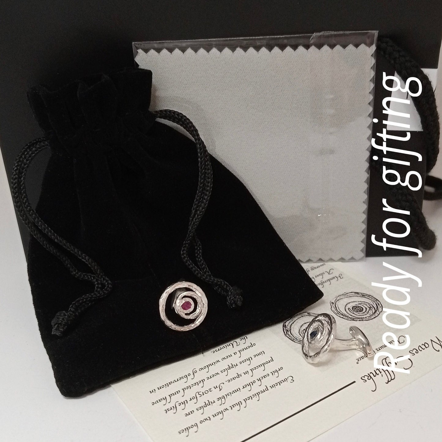 Set de regalo de gemelos de plata artesanales con zafiro y rubí, bolsa de terciopelo negro y tarjeta informativa sobre el diseño.