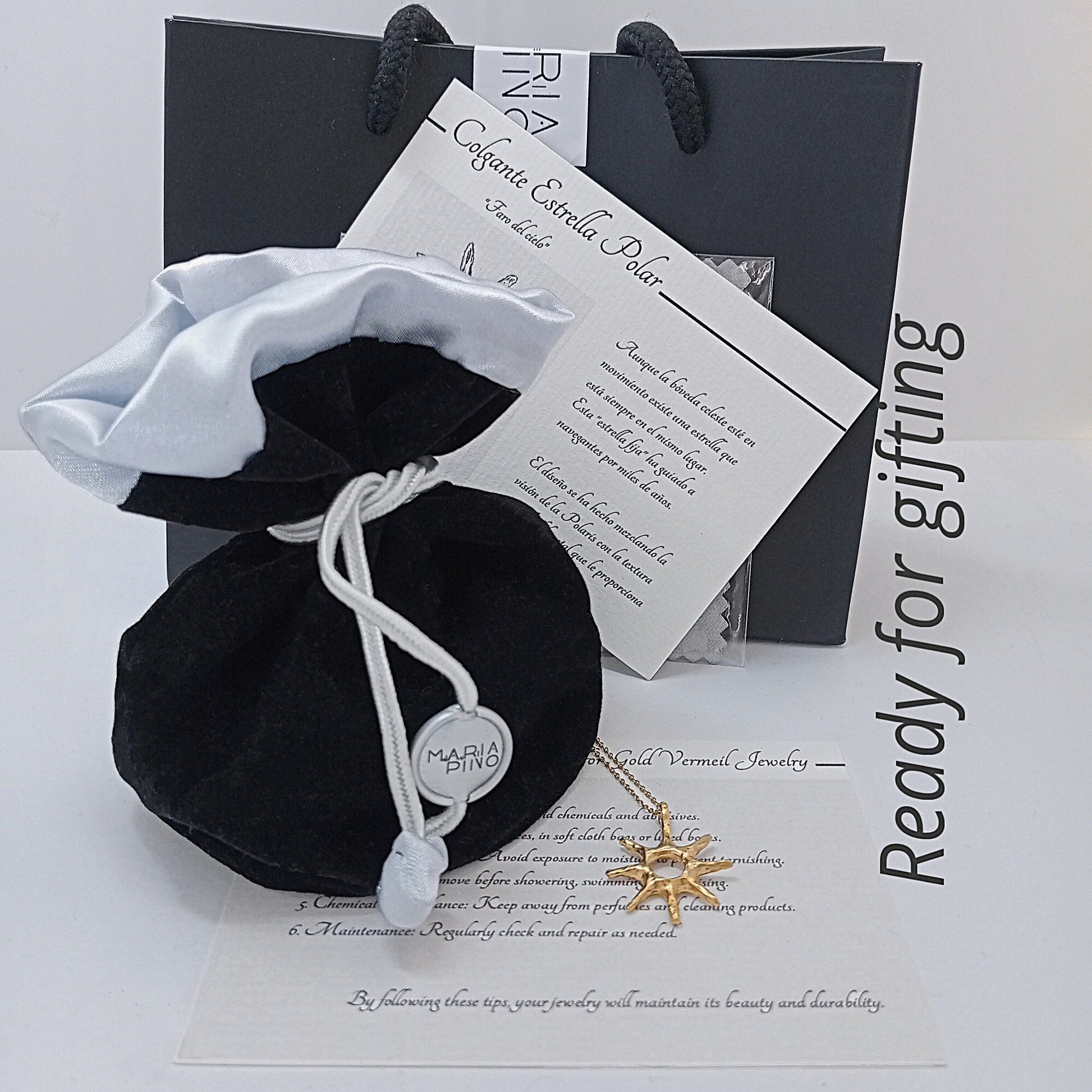 Set de regalo de joyería con bolsa de terciopelo negro, tarjeta de significado "Faro del Cielo" y bolsa de marca María Pino.