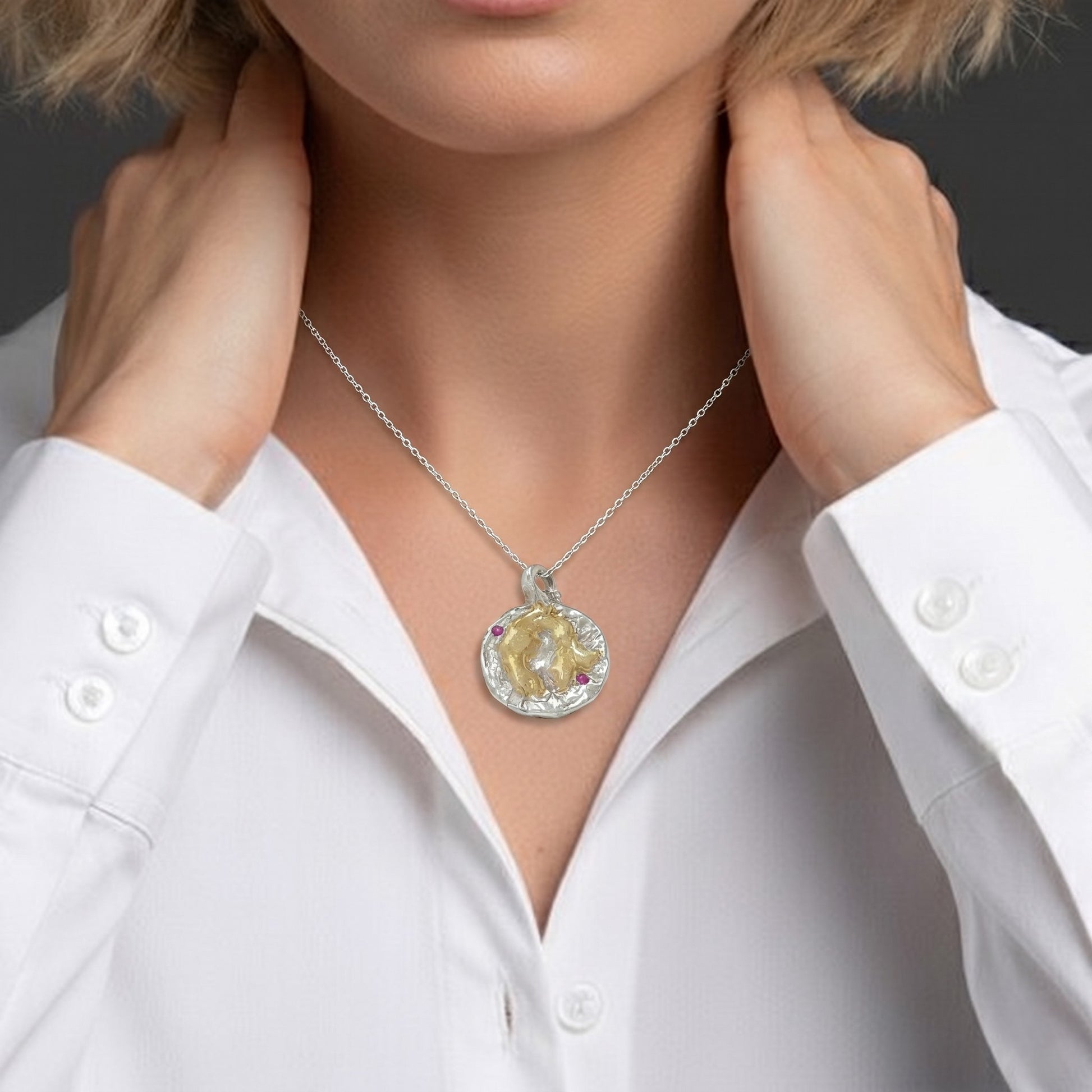 Modelo llevando colgante artesanal de plata y oro vermeil con dos rubíes naturales sobre camisa blanca.