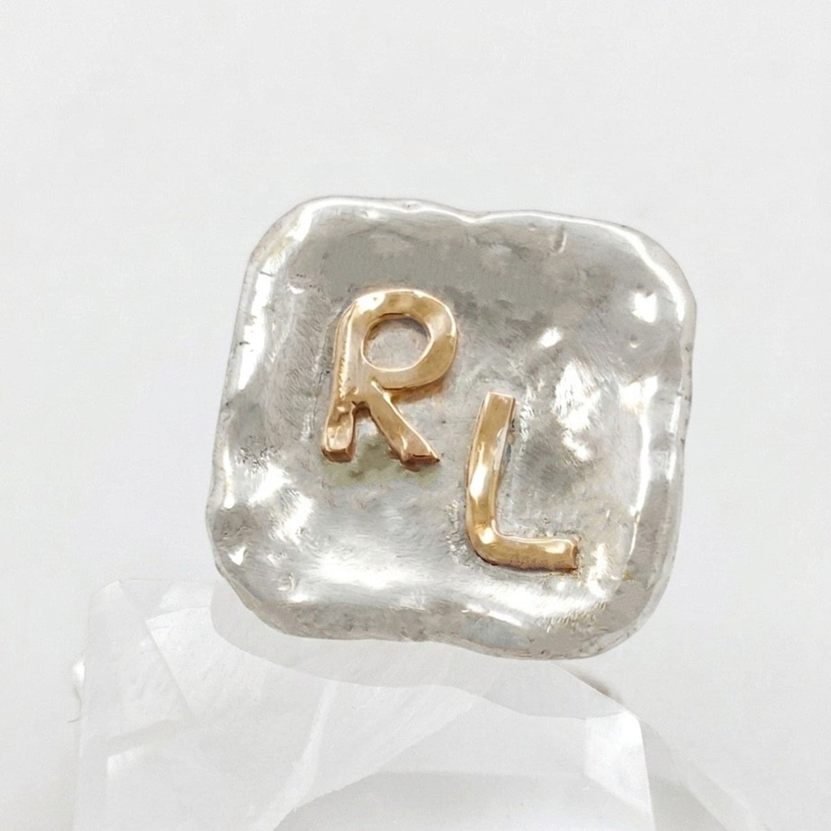 Primer plano de un gemelo de plata con las iniciales RL en oro de 18 k y textura orgánica