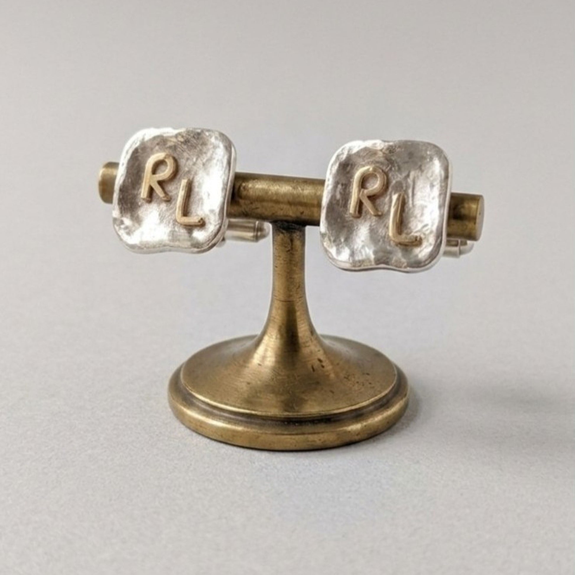 Gemelos personalizados de plata con iniciales RL en oro de 18K expuestos sobre un soporte de joyería. 